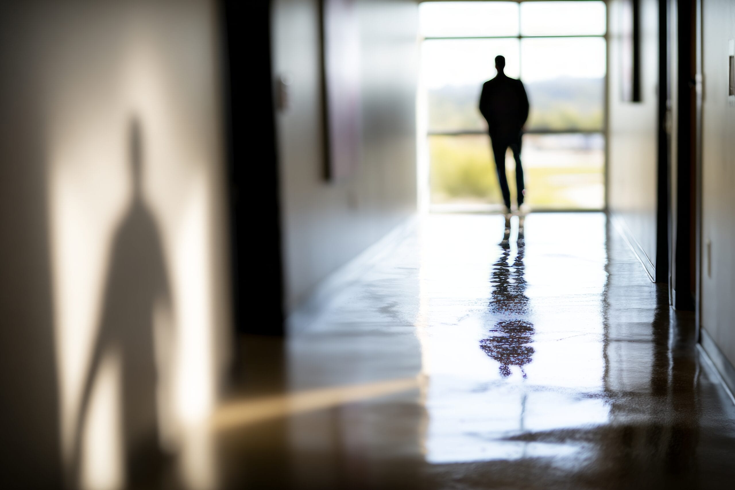 Silhouette of person walking down bright corridor toward window